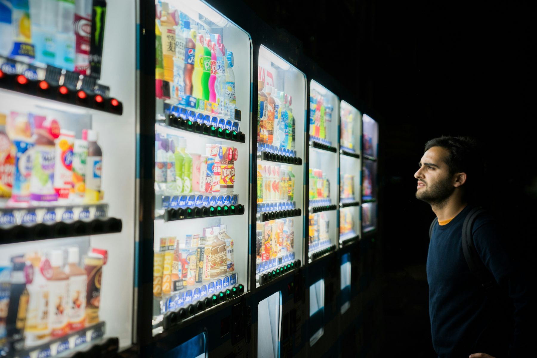 A man looking at vending machines stocked full of snacks and drinks.