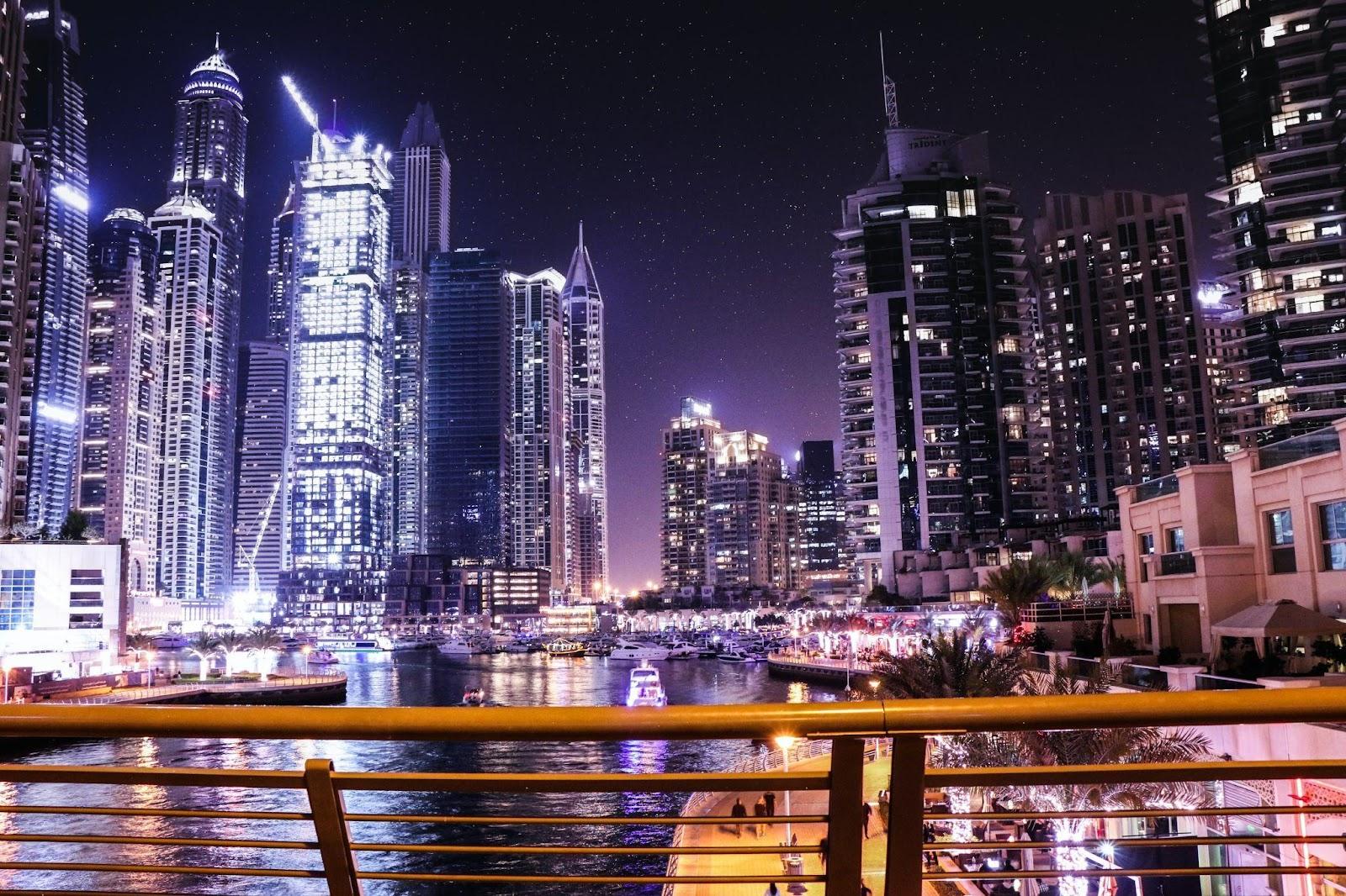 A picture if Dubai at night, featuring lit up buildings behind a lake.