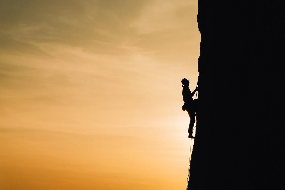 Image of rock climber with positive mindset climbing a mountain at sunrise