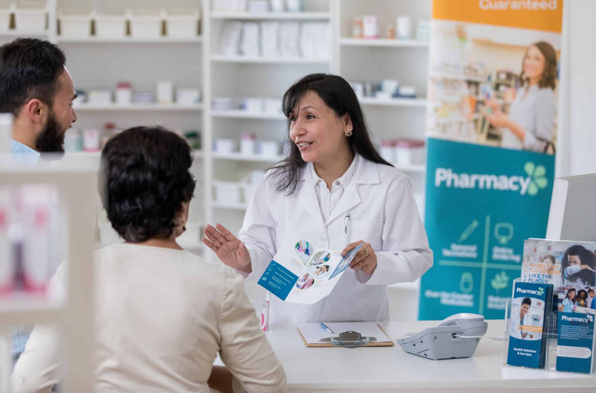 Pharmacist Working In Pharmacy With Customer