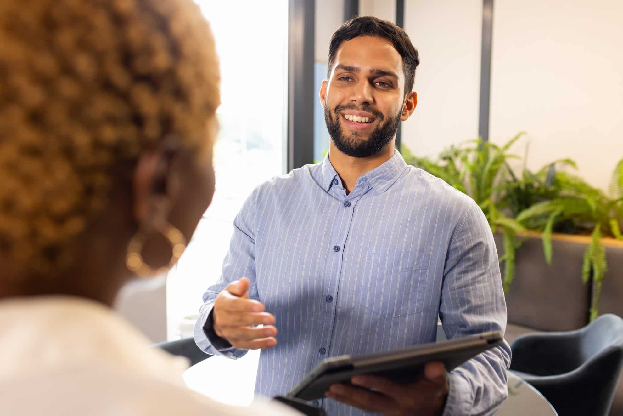 Smiling business professional holding a tablet and greeting a new client during a meeting in a modern UAE office setting.